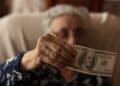 Elderly woman holding a $100 bill as part of the $900 heating assistance program in New York, 2025