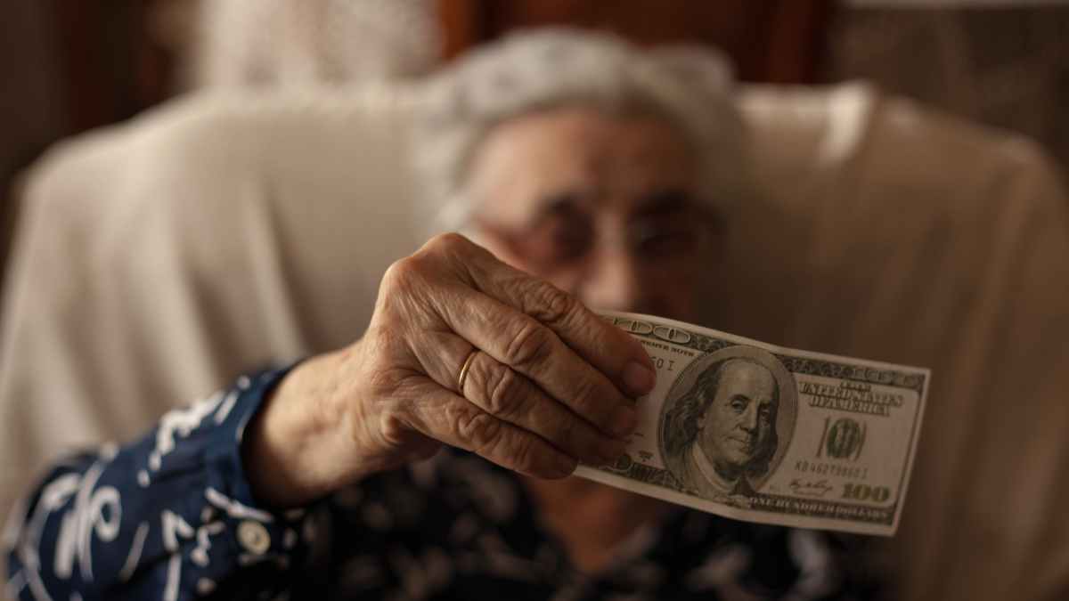 Elderly woman holding a $100 bill as part of the $900 heating assistance program in New York, 2025