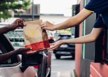 McDonald's job opportunities: employee handing food to customer at drive-thru window. Fast food employment with flexible shifts and benefits