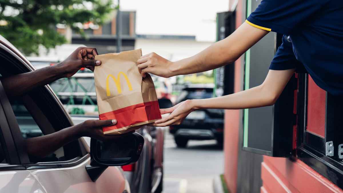 McDonald's job opportunities: employee handing food to customer at drive-thru window. Fast food employment with flexible shifts and benefits