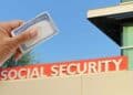 Social Security card in hand in front of the Social Security office, representing cuts in retirement benefits