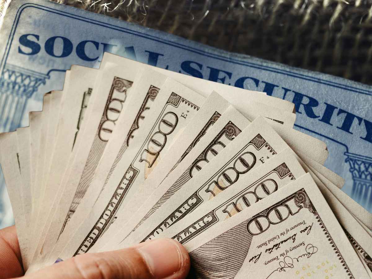 Hand fanning out $100 bills over a Social Security card, symbolizing $2,000 Social Security payment conditions for May 14 2025
