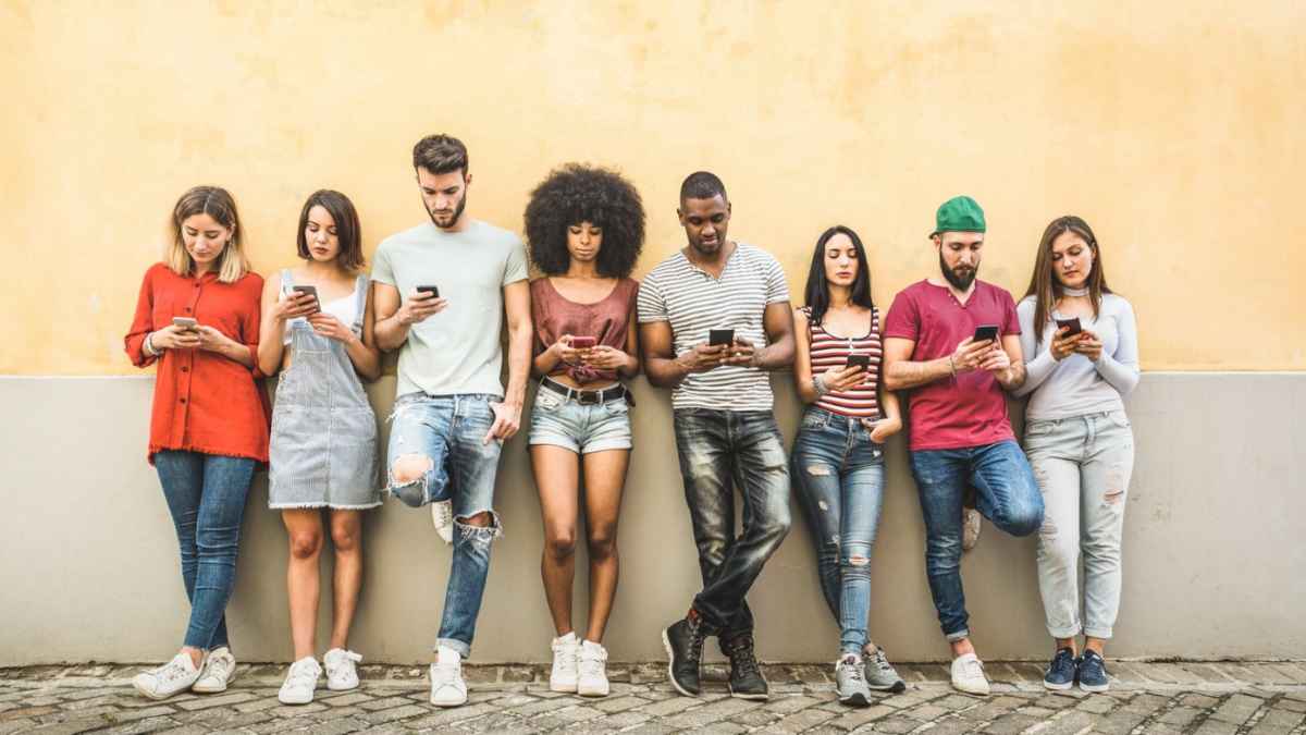 Group of diverse Gen Z young adults standing against a wall using smartphones, reflecting youth unemployment and digital engagement