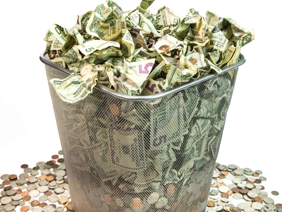 Crumpled U.S. dollar bills overflowing from a trash can symbolizing global decline of the dollar in 2025