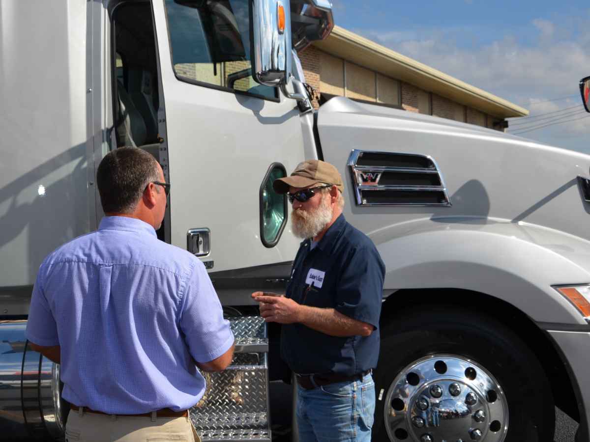 Two commercial truck drivers beside a white semi-truck discuss FMCSA deadline for replacing 15,000 revoked medical certificates
