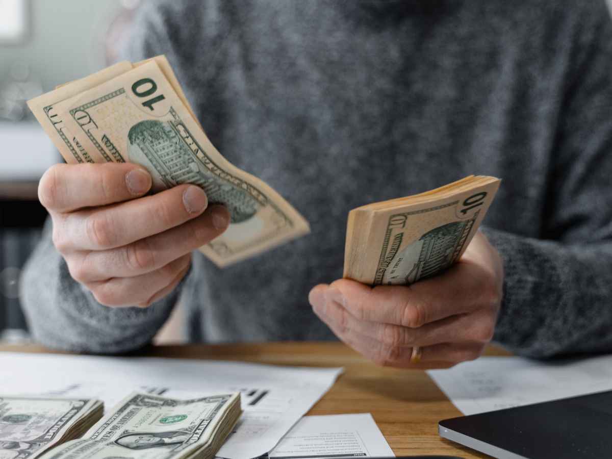 Person counting ten-dollar bills at a desk with paperwork, illustrating the upcoming $1,450 SSI payment on May 1 for eligible beneficiaries