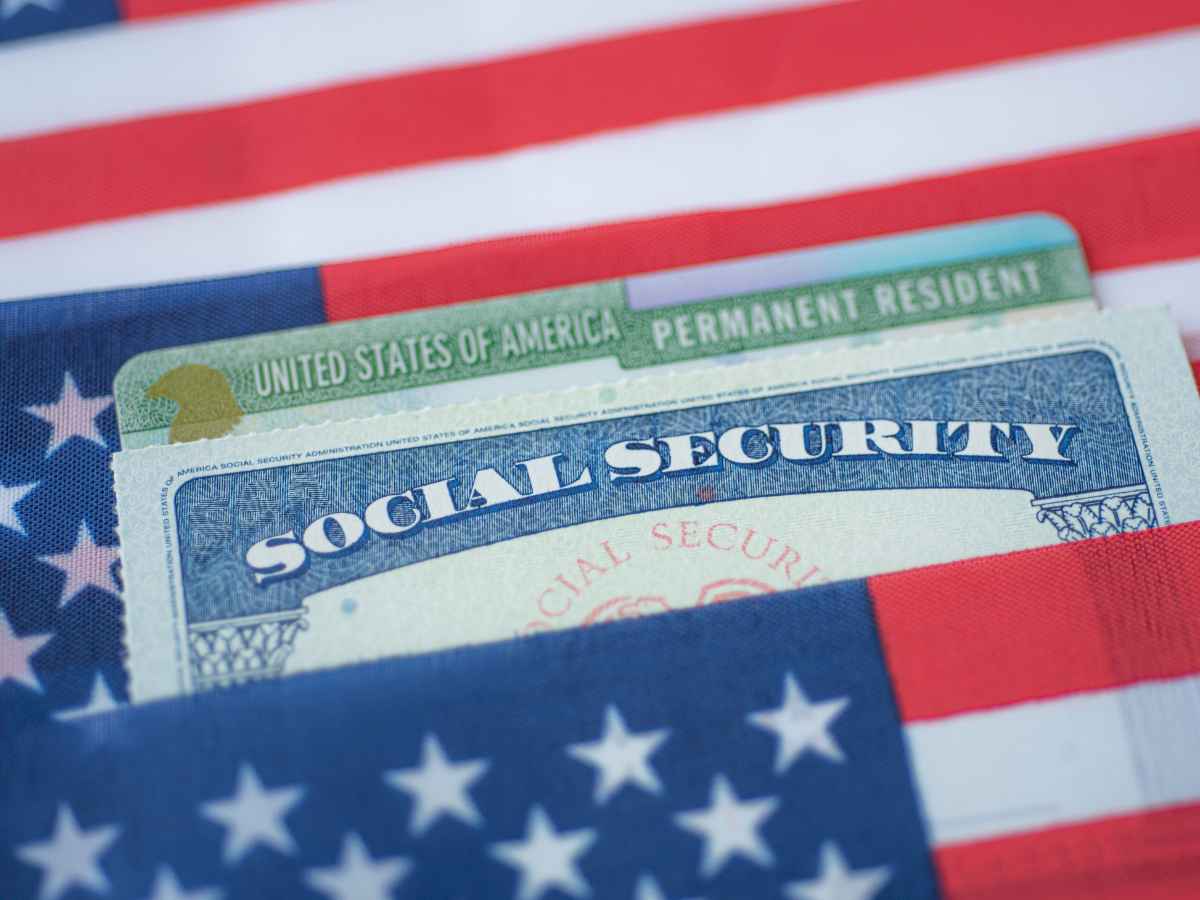 “Close-up of a U.S. Social Security card and Permanent Resident card against an American flag background”