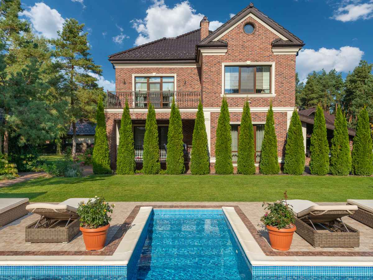 Two-story brick house with balcony, manicured evergreens, and private pool—illustrating the $600K dream-home upgrade a retired couple is considering in an amenity-rich community