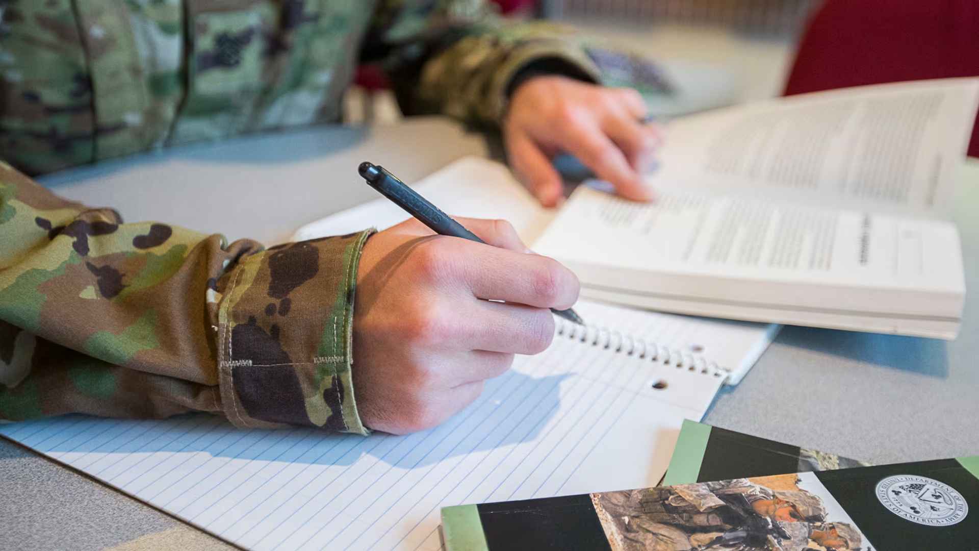 Veteran in camouflage taking notes with textbook while using 90 percent Post-9/11 GI Bill (Chapter 33) education benefits