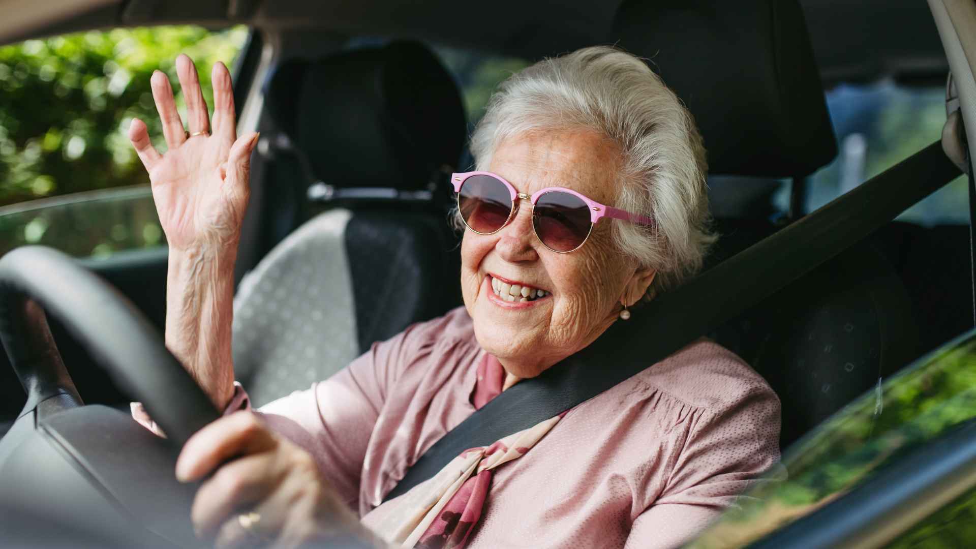 Senior California driver waves while behind the wheel, illustrating new DMV license-renewal rules for older motorists