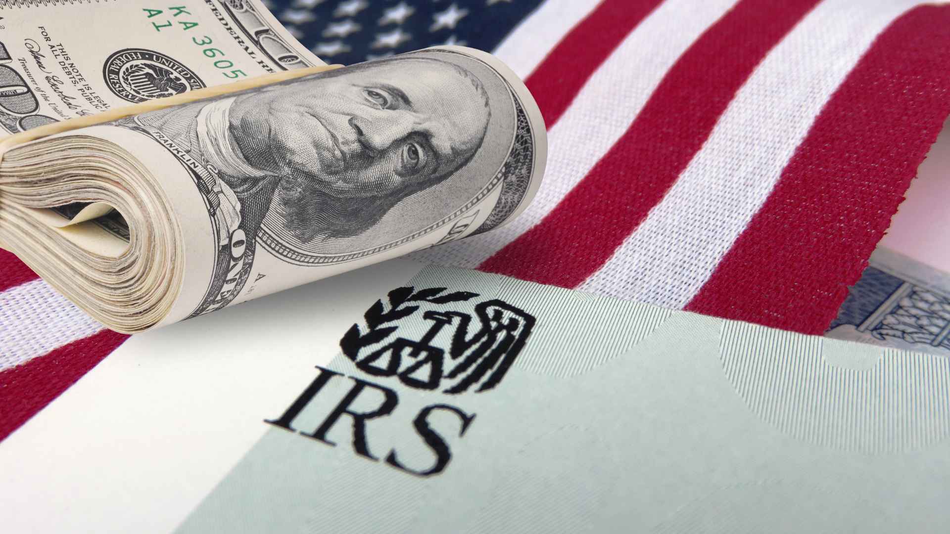 Rolled hundred-dollar bill on an IRS notice beneath the U.S. flag, symbolizing the risk of bank-account seizure for unpaid taxes.