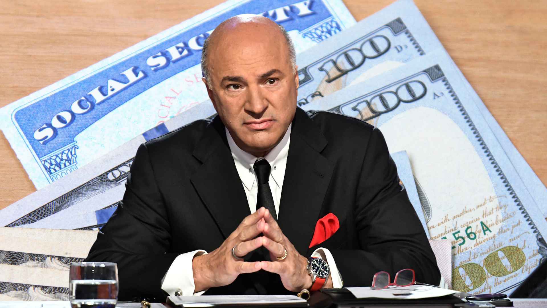 Kevin O’Leary seated at a desk with a Social Security card and $100 bills backdrop, emphasizing retirement savings needs