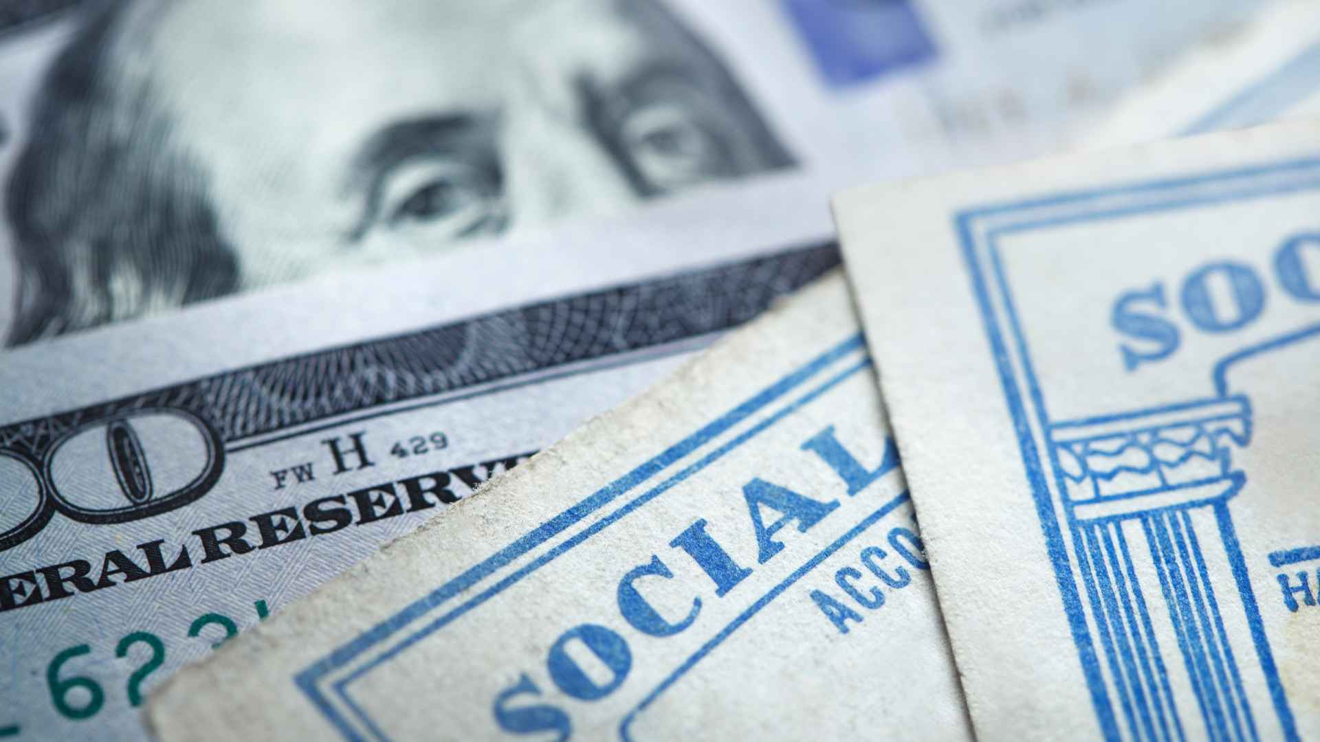 Social Security cards lying on $100 bills, representing millionaire and billionaire eligibility for benefits.