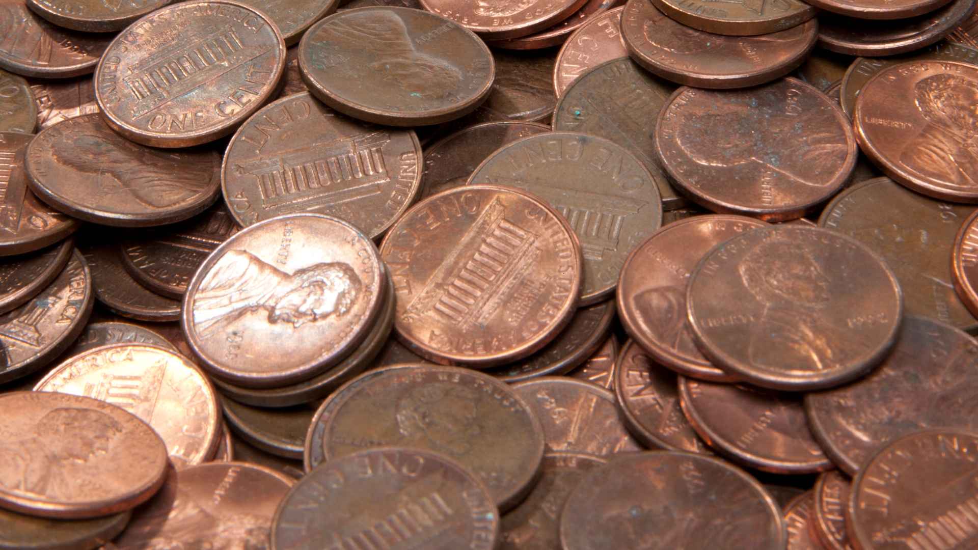 Close-up of scattered U.S. pennies showing Lincoln and the Lincoln Memorial, highlighting the rising minting costs behind their phase-out.