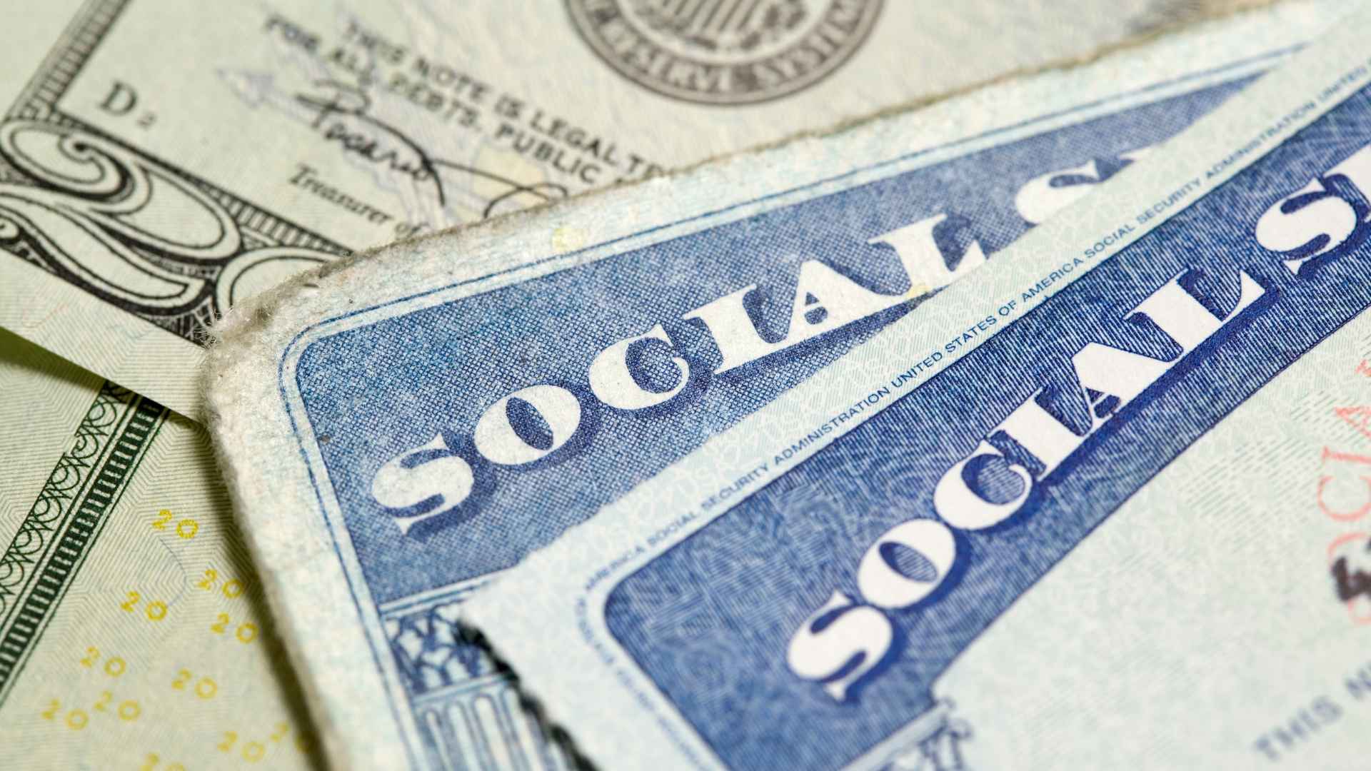 Close-up of Social Security cards on U.S. dollar bills illustrating higher retirement age and delayed full benefits.