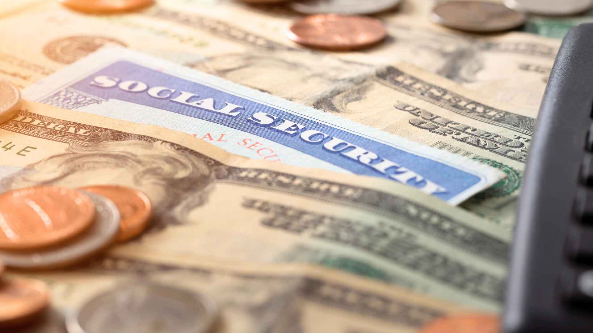 Close-up of a Social Security card on U.S. dollar bills and coins symbolizing June 2025 benefit payments averaging $1,976