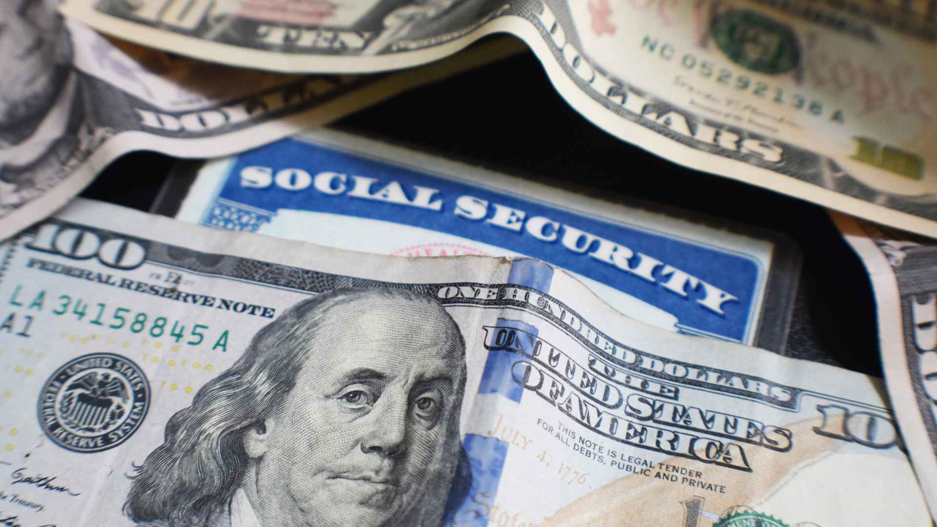 Stack of U.S. $100 bills covering a Social Security card, illustrating the June SSI check arriving early in May.