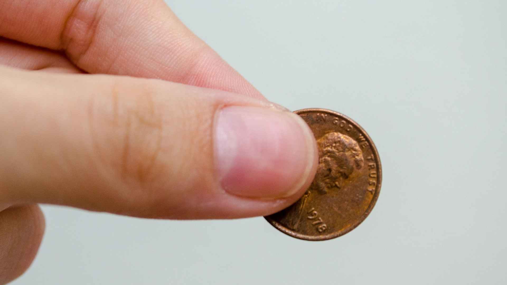 Hand holding a close-up of a Lincoln penny, symbolizing the search for rare 1943 copper coins