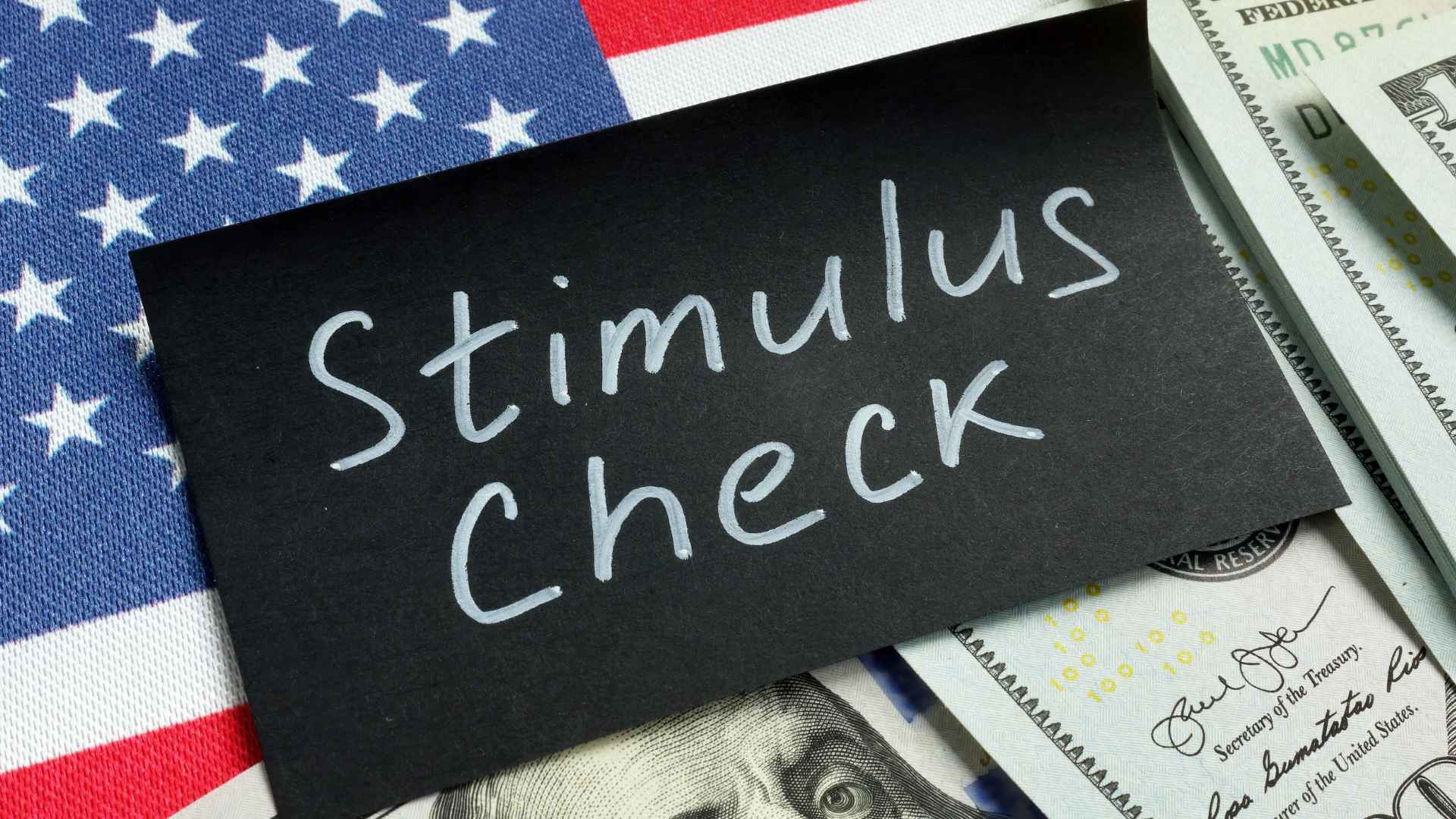 Handwritten “Stimulus Check” card on U.S. flag and $100 bills, illustrating new $500 payment eligibility.