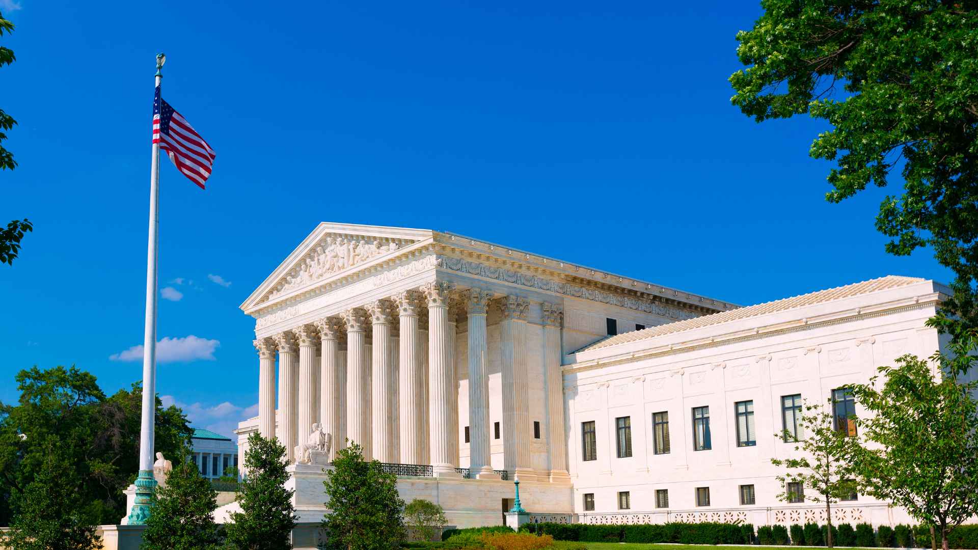 U.S. Supreme Court building with American flag against a clear blue sky, symbolizing the justices’ landmark ruling