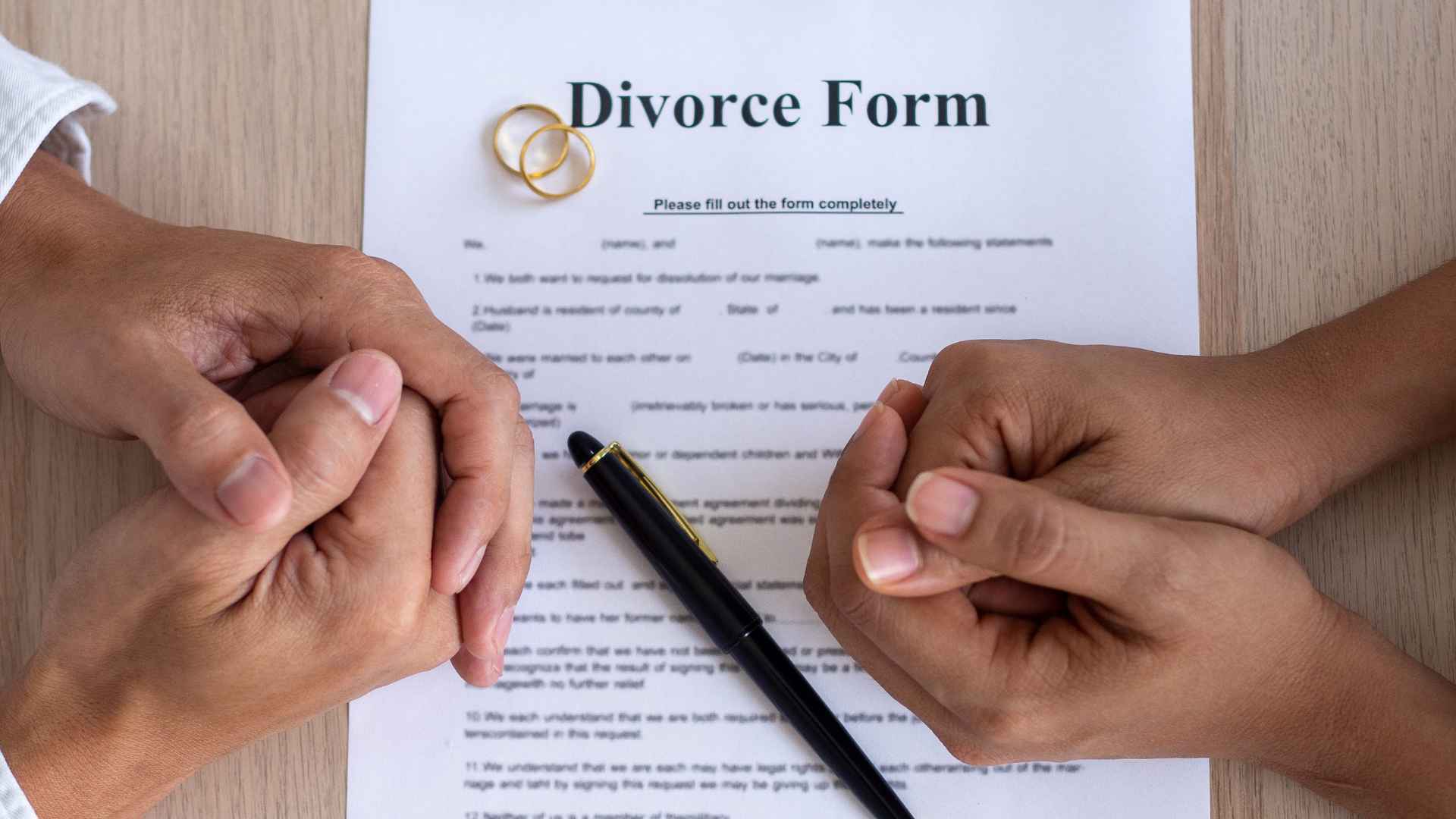 Two people facing each other over a divorce form with wedding rings and a pen on the table