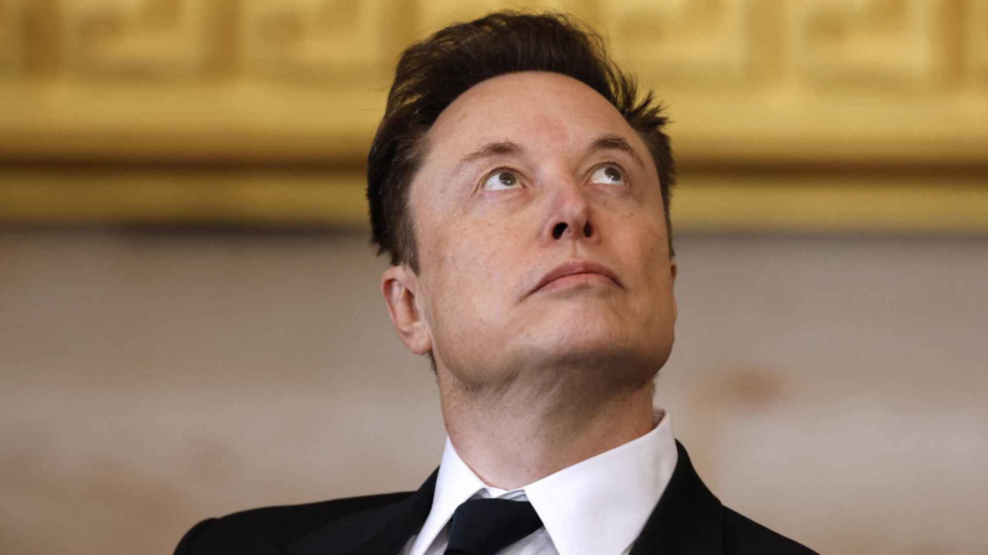 Close-up of a suited business executive looking upward during a formal event, with a soft golden backdrop