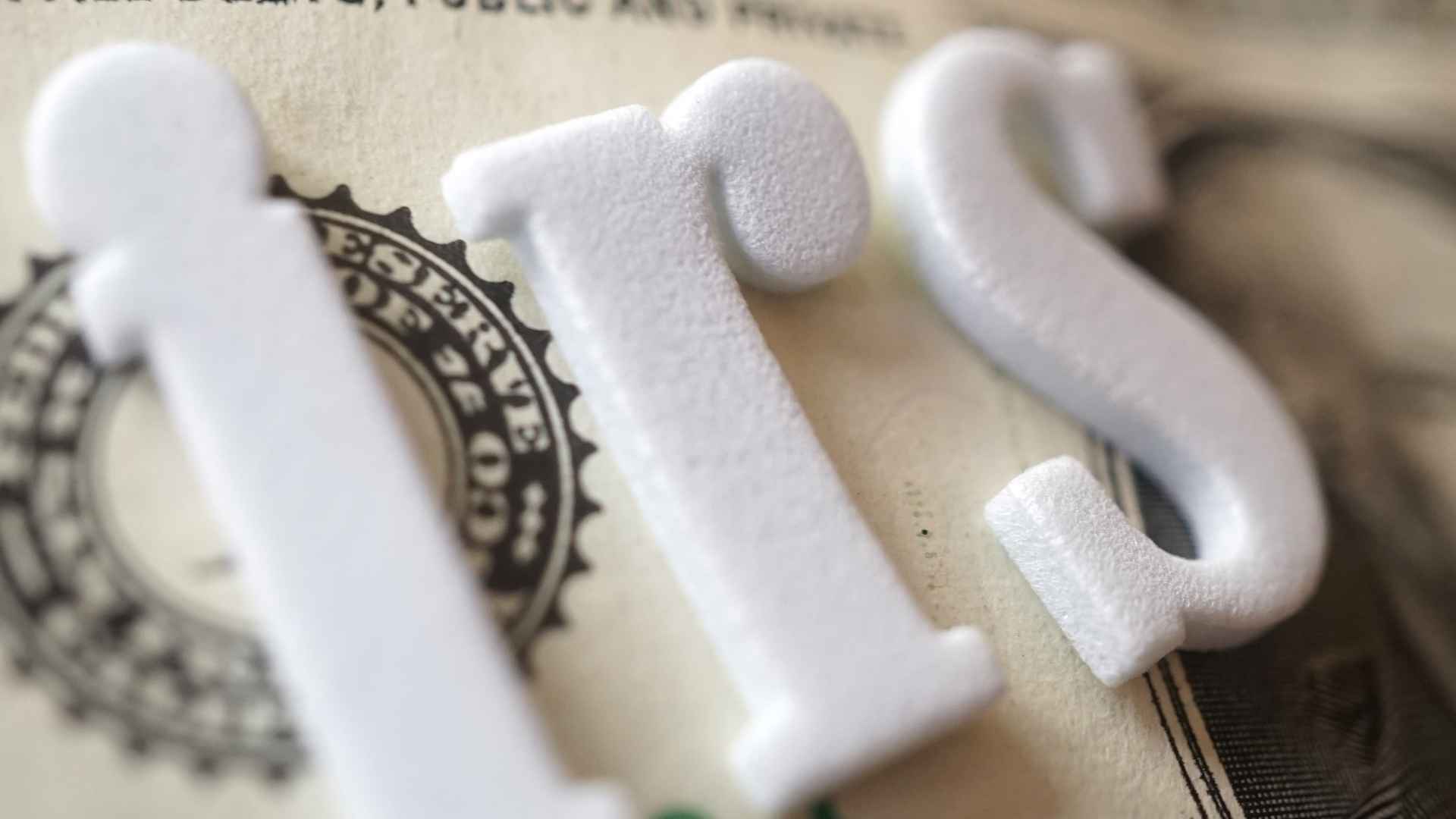 IRS letters on dollar bill symbolizing government property seizures for unpaid 2025 tax debts