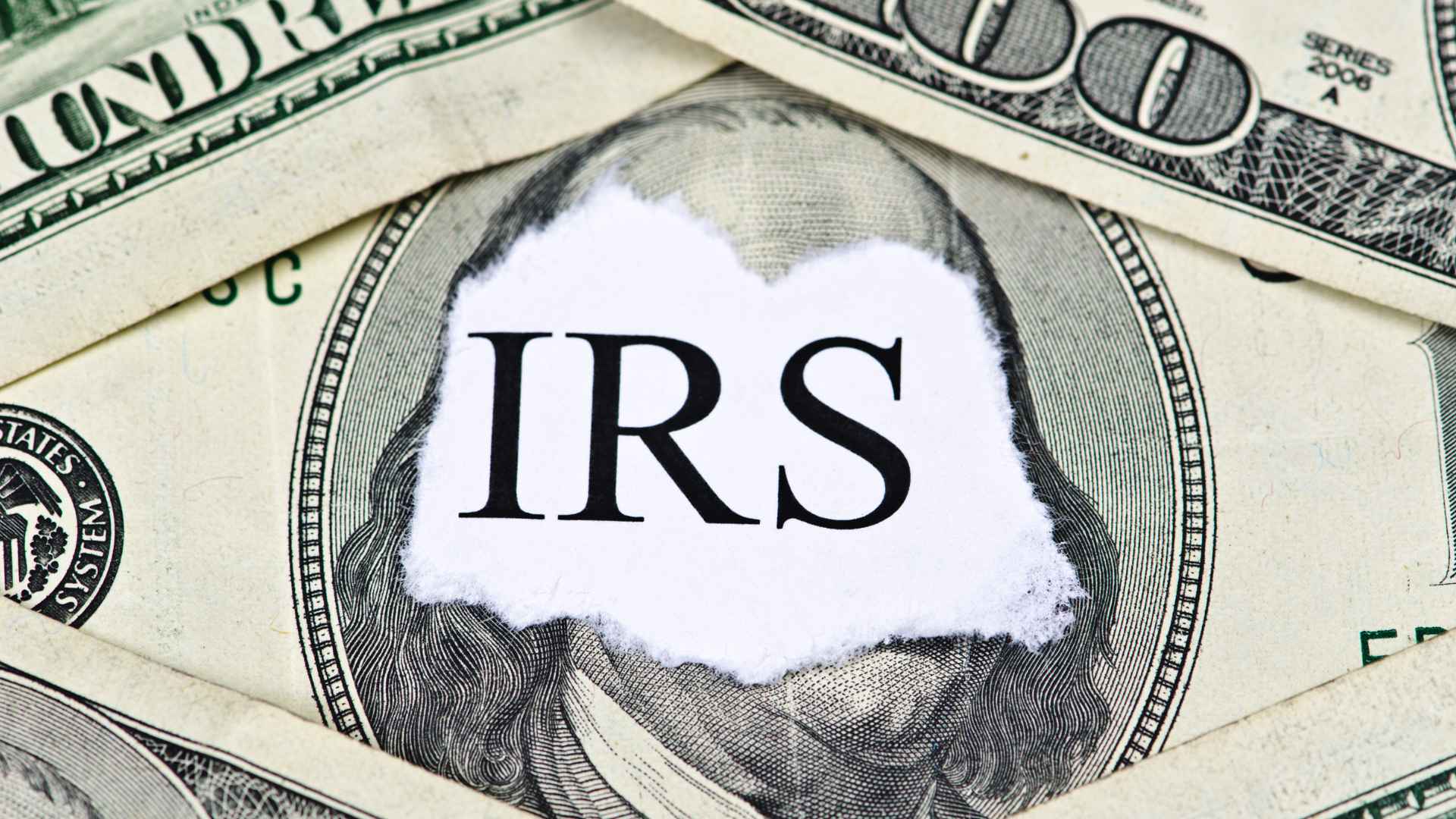 Torn paper reading “IRS” over a U.S. hundred-dollar bill, symbolizing overseas taxpayers’ June 16 2025 tax-filing deadline.