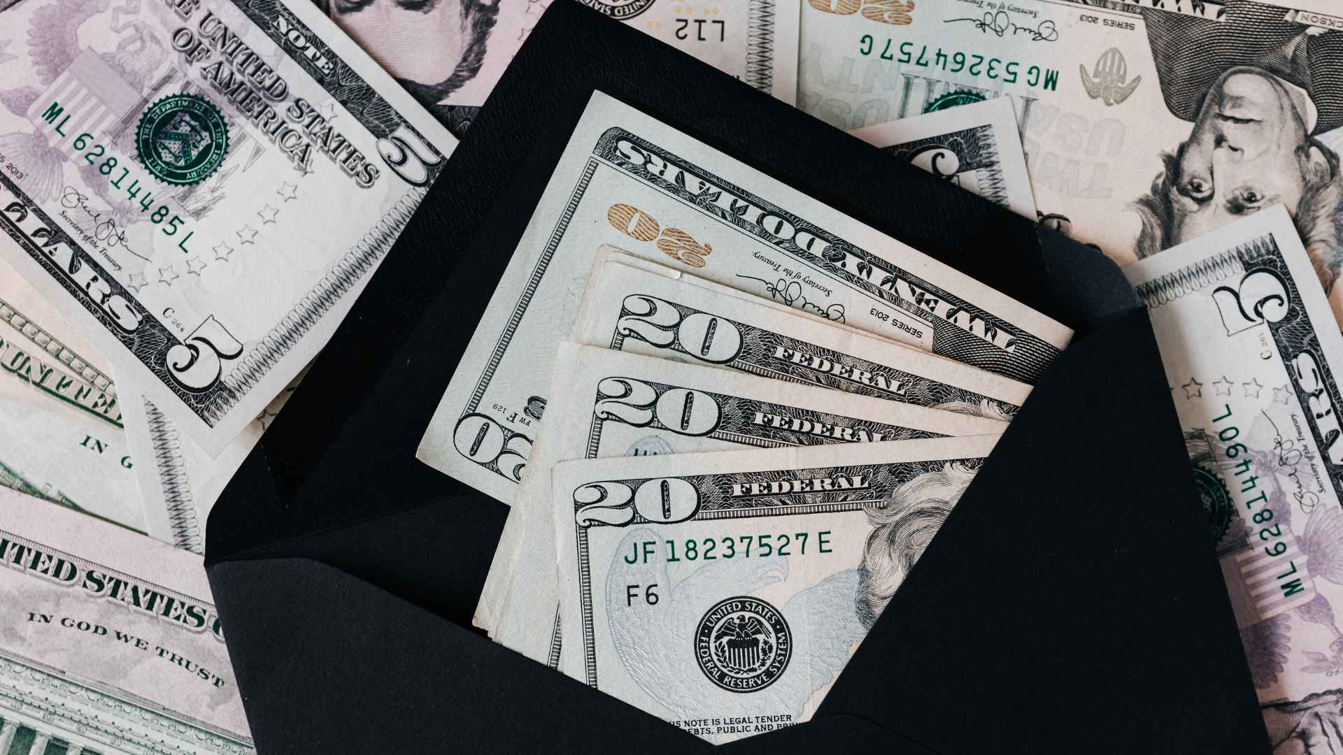 U.S. twenty-dollar bills spilling from a black envelope, symbolizing the new aid checks headed to eligible citizens this month.