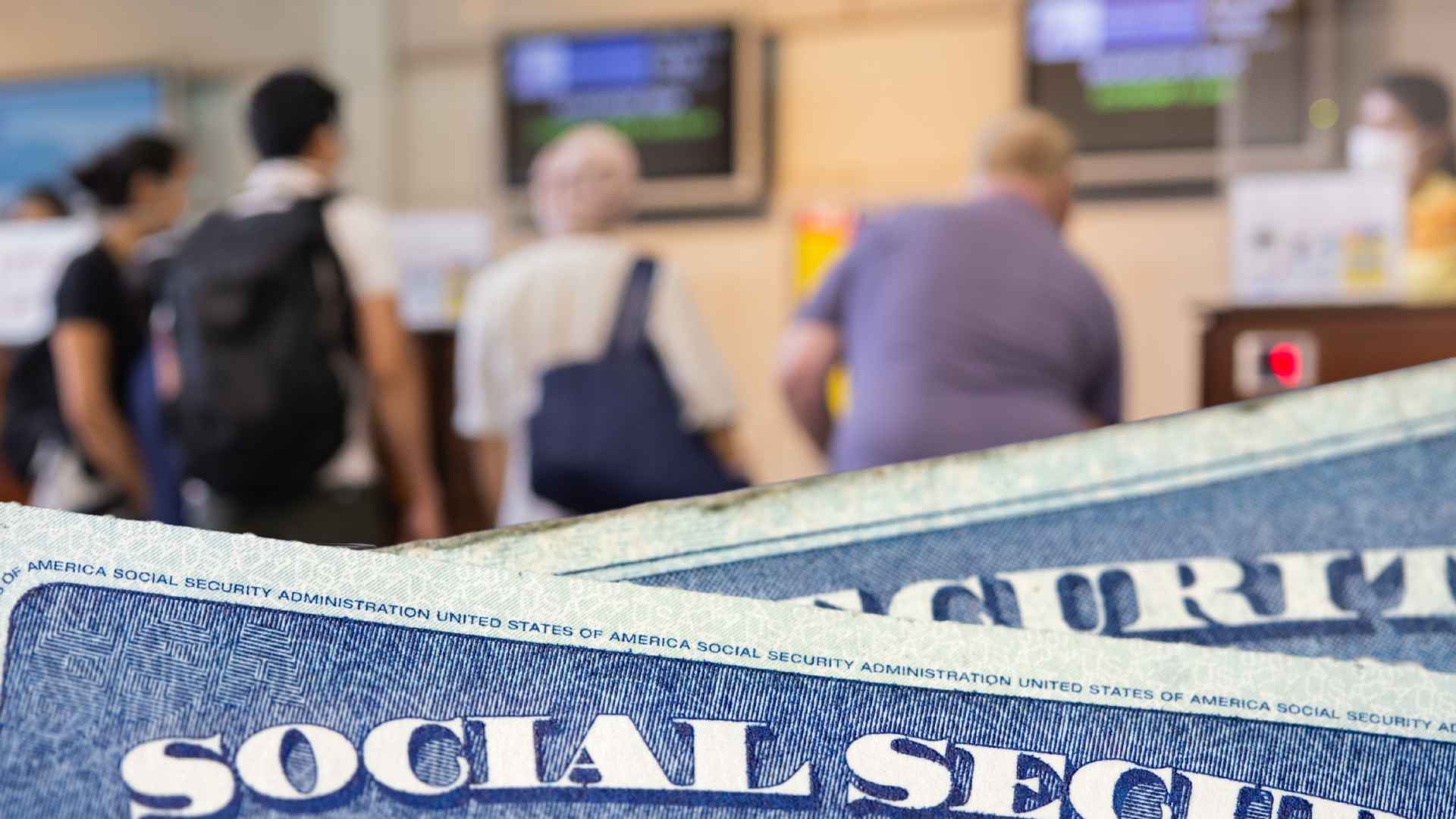 Close-up of Social Security cards with retirees waiting at an SSA office, illustrating the payout gap and shifted benefit schedule.