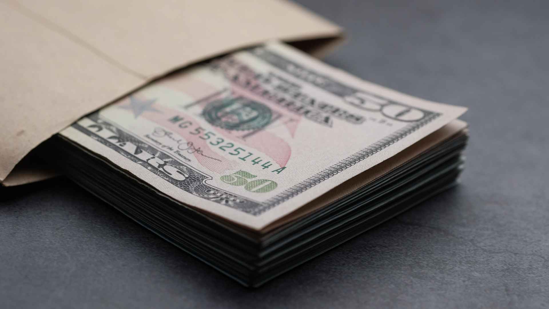 Stack of $50 bills peeking from a brown envelope, illustrating Richmond’s $3.9 million housing relief grant for eligible residents.