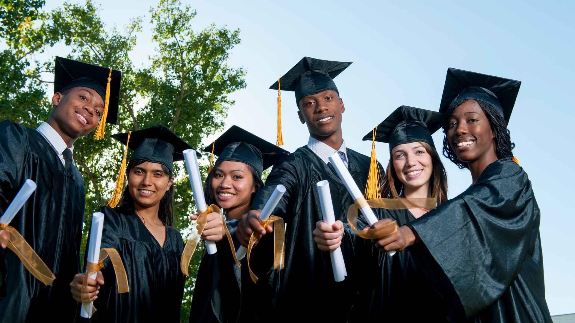 Group of diverse international students celebrating graduation, holding diplomas in caps and gowns outdoors