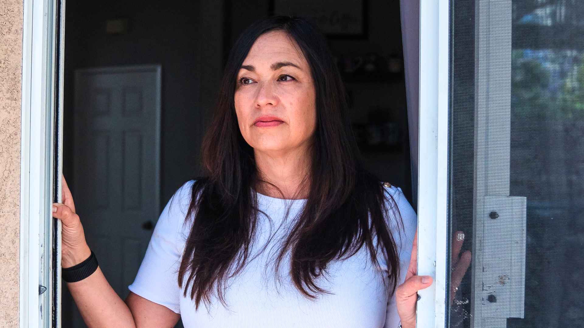 Woman looks out from doorway, concerned about federal retirement cuts after 35 years of Social Security service