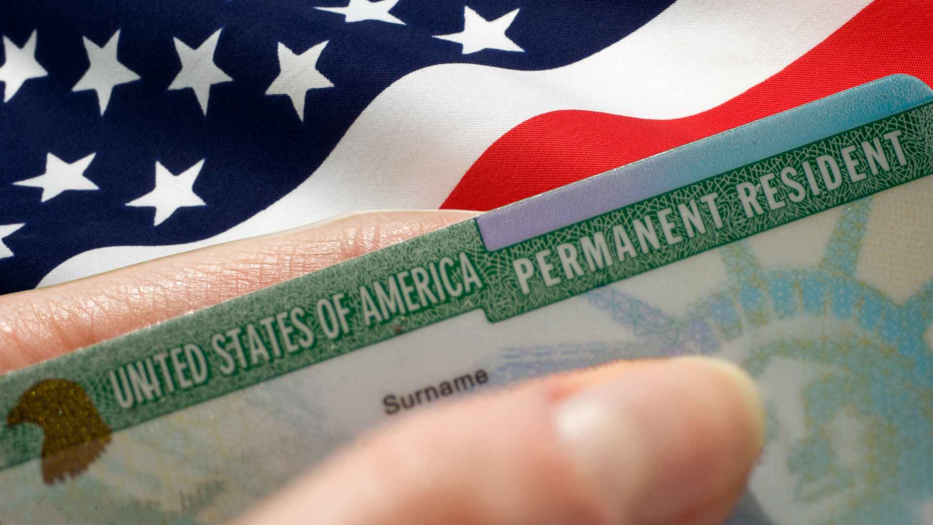 U.S. green card held against an American flag, illustrating tighter health subsidies and new 1 % remittance fee under Trump’s One Big Beautiful Bill.