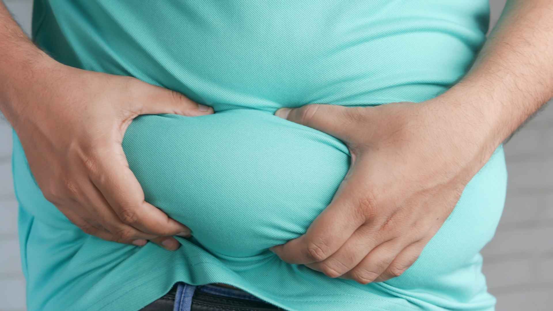 Person gripping their stomach to highlight excess belly fat as part of fitness goals and exercise routine.