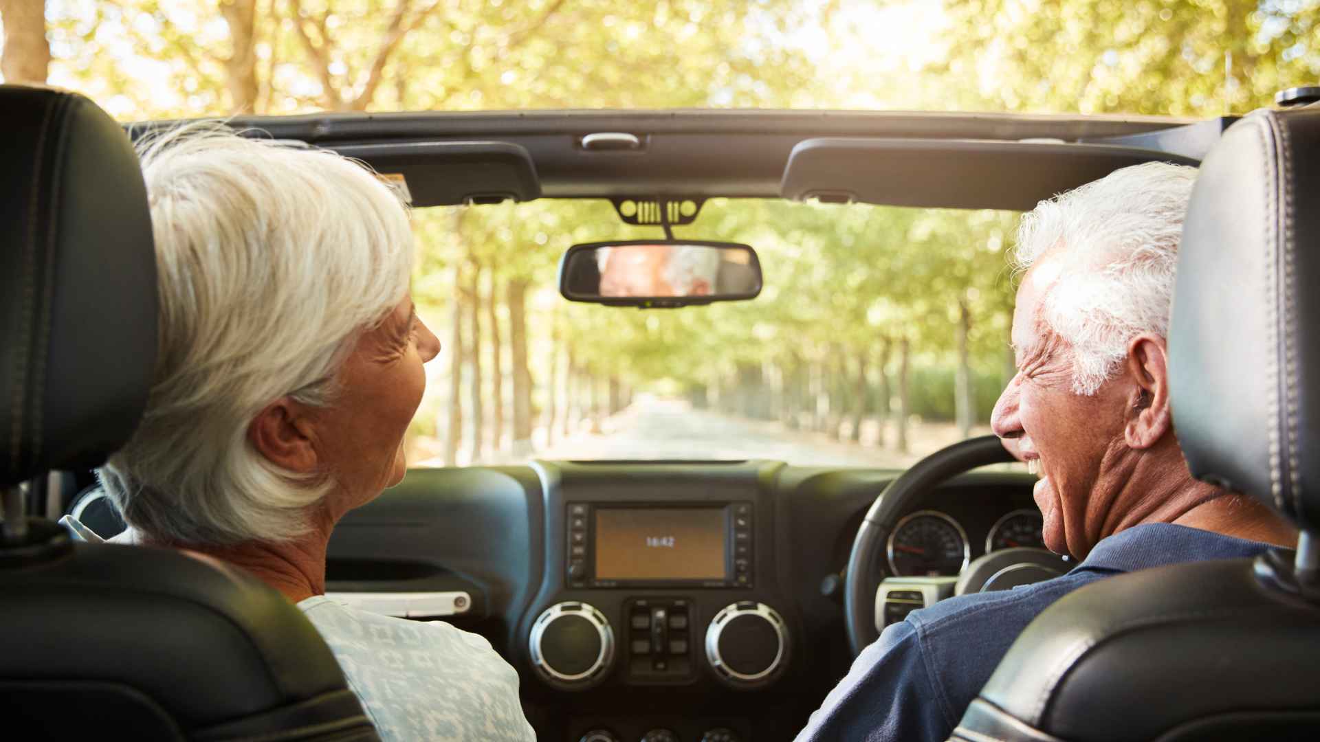 Senior couple driving a car on a sunny day, smiling and enjoying the ride together