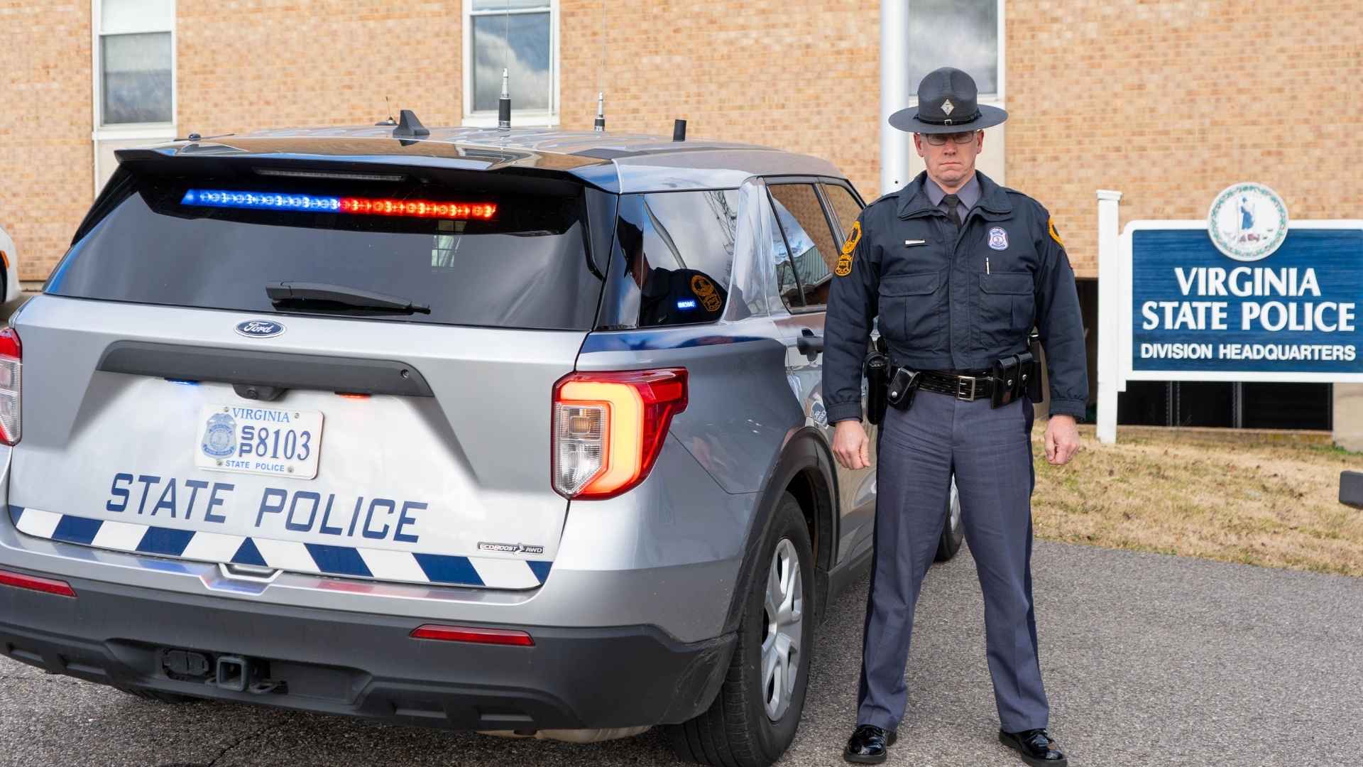 Virginia State Police officer standing next to patrol vehicle enforcing new $25 seatbelt fine law for passengers.
