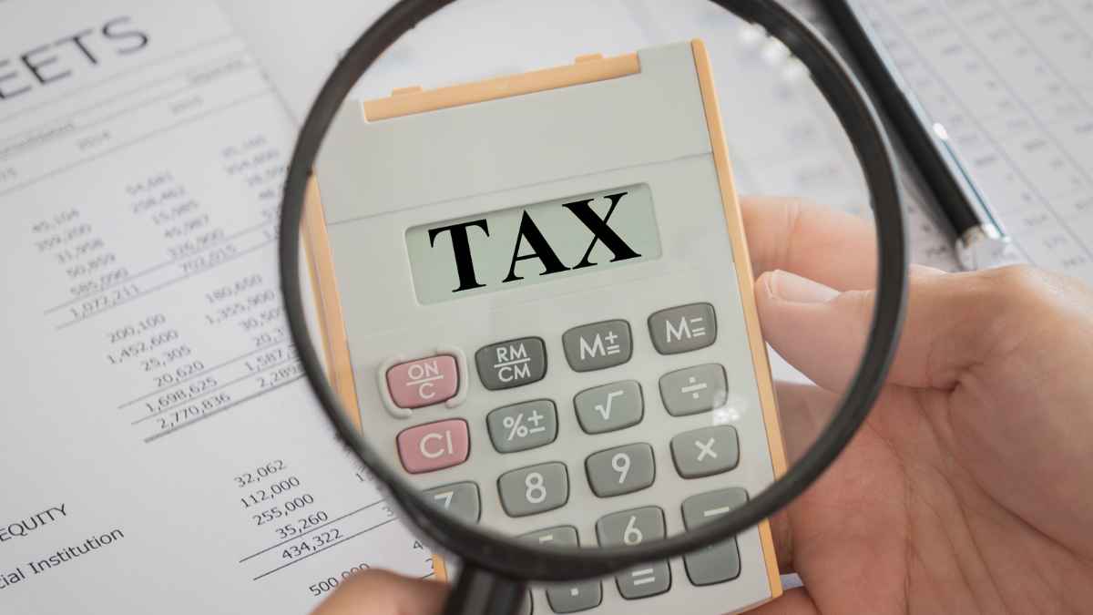 Calculator with magnifying glass highlighting the word 'TAX' on financial documents.
