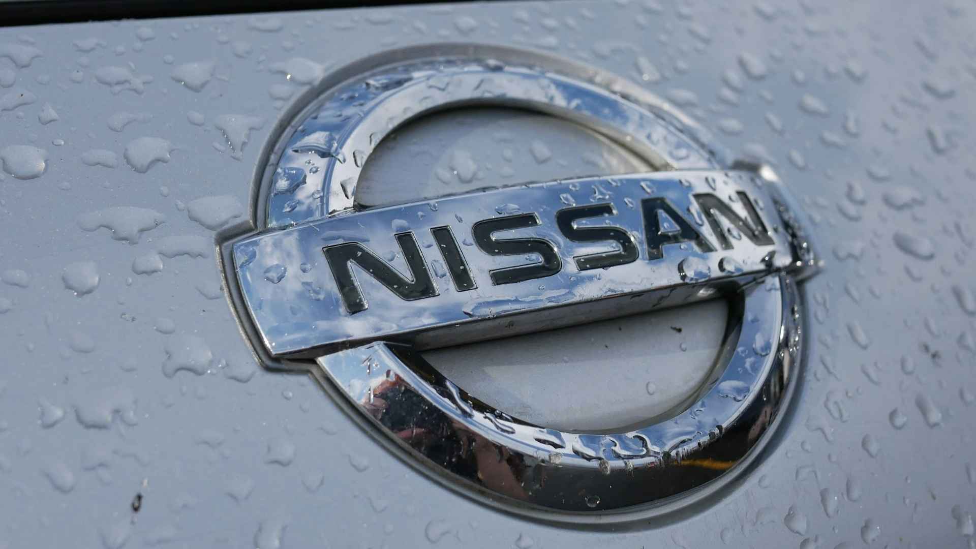 Nissan logo close-up on a silver car with water droplets, symbolizing the brand's recall of 480,000 vehicles
