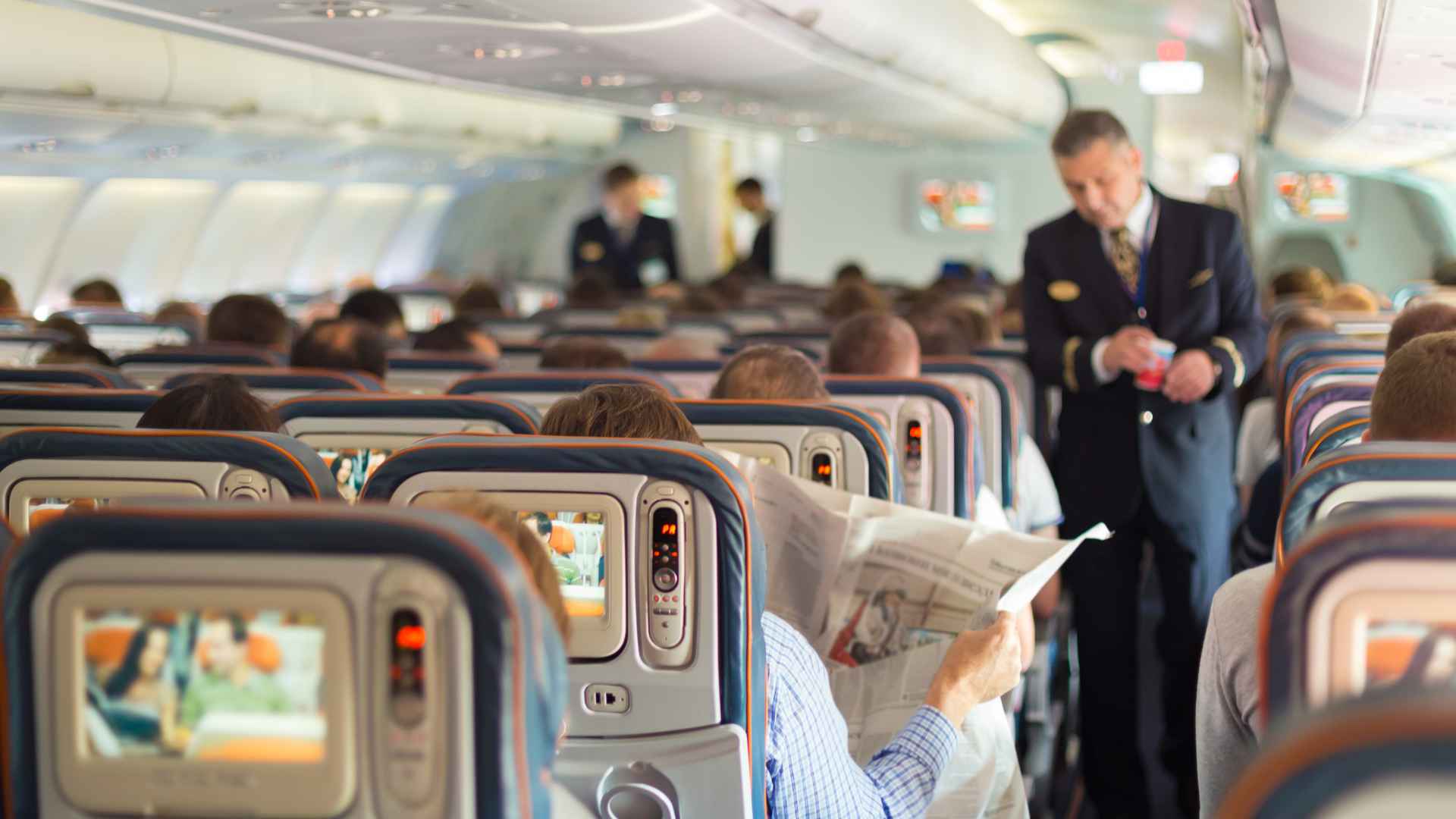 Passengers seated on a commercial airplane with flight attendants serving, representing airplane etiquette and seat assignments.