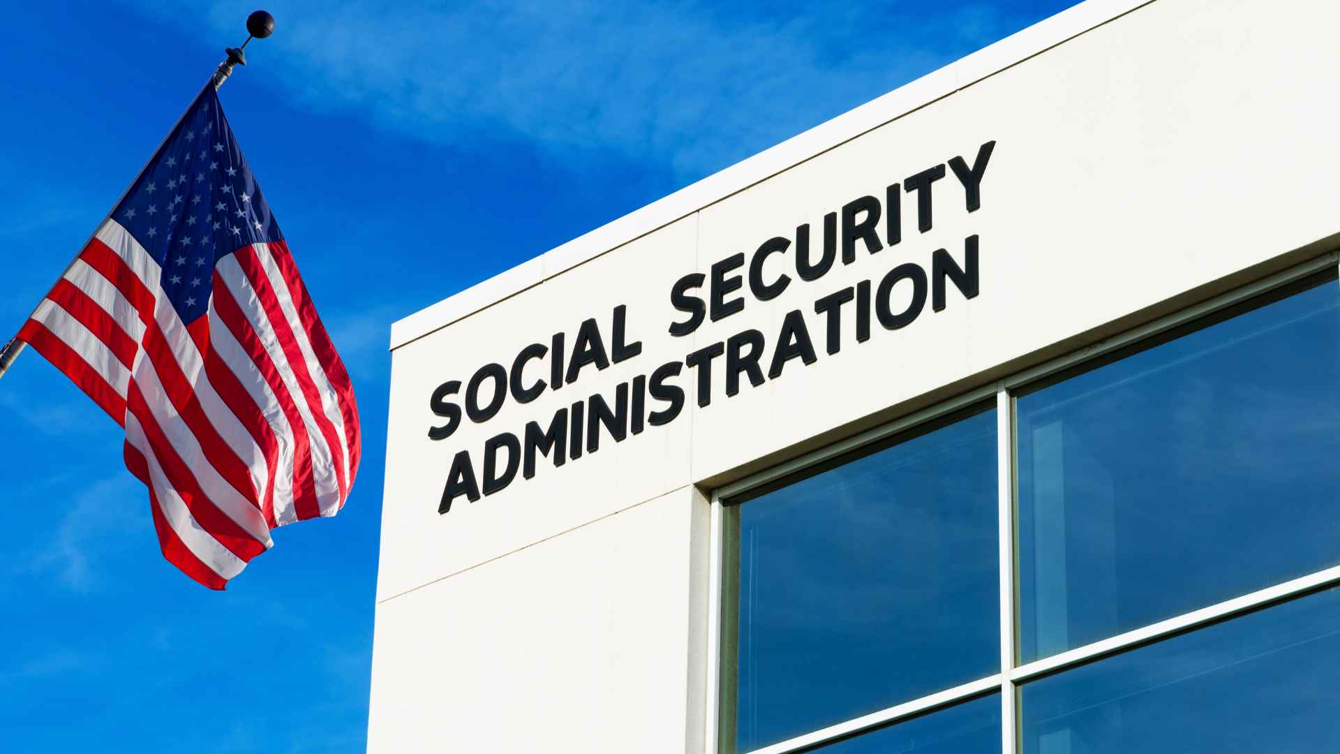 Social Security Administration building with American flag in the background against a clear blue sky