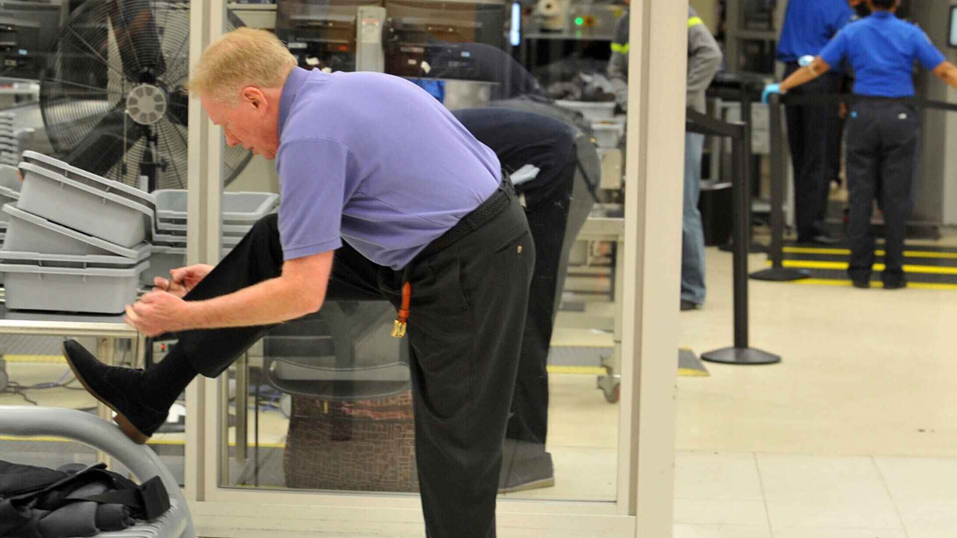 Traveler removing shoes at TSA airport security checkpoint prior to new rule allowing shoes-on screening.