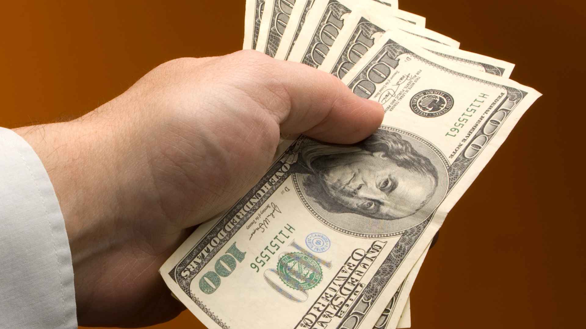 Hand holding cash in $100 bills symbolizing $600 tariff rebate checks proposed in Congress