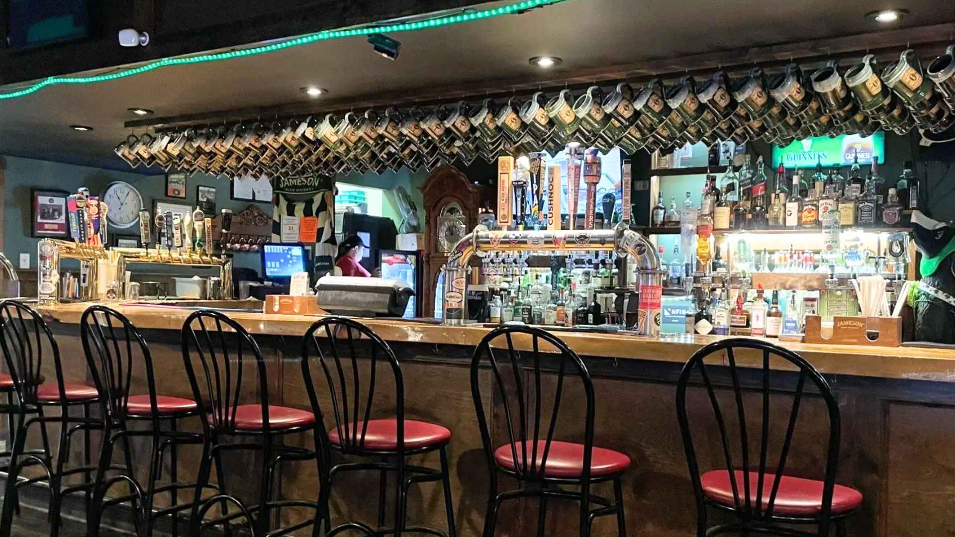 Interior view of John Sullivan’s Irish pub showing empty bar stools, hanging mugs and beer taps