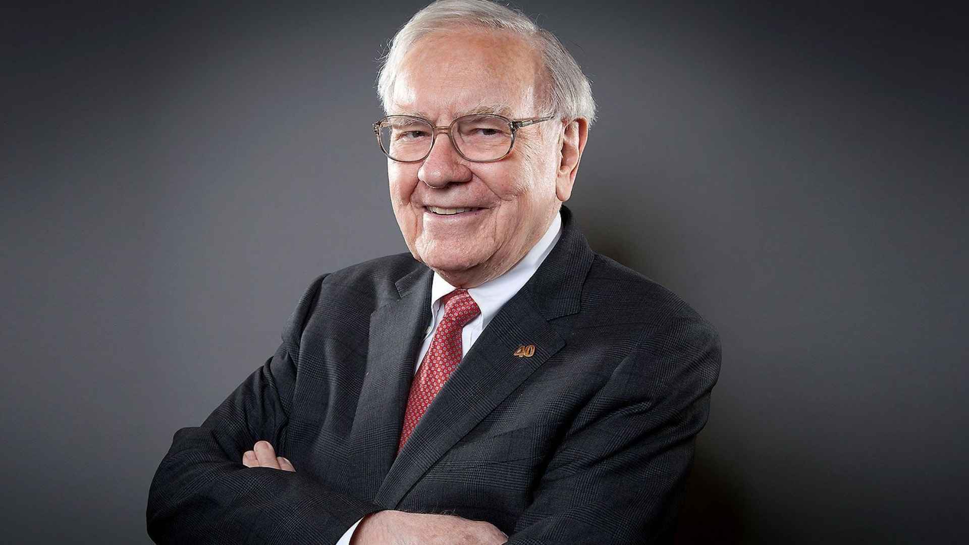 Warren Buffett smiling in a suit and red tie discussing buying homes at bargain prices with long-term mortgages