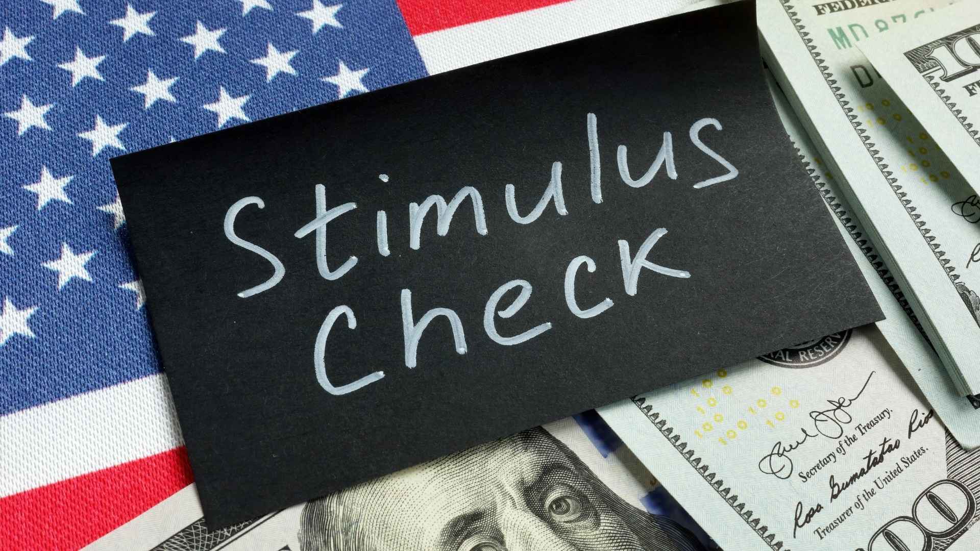 Stimulus check note on American flag background with US dollar bills underneath