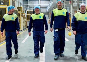 Cuatro operarios de producción con uniforme azul y chaleco amarillo caminan por el interior de la fábrica de Caiba, especializada en envases de plástico, en Las Ventas de Retamosa (Toledo).