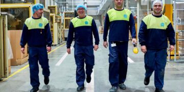 Cuatro operarios de producción con uniforme azul y chaleco amarillo caminan por el interior de la fábrica de Caiba, especializada en envases de plástico, en Las Ventas de Retamosa (Toledo).