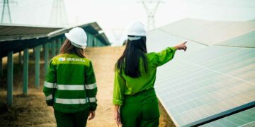 Dos empleadas de Iberdrola supervisando paneles solares en un proyecto de energía renovable con uniformes corporativos