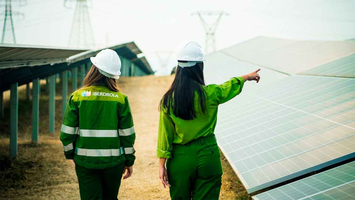 Dos empleadas de Iberdrola supervisando paneles solares en un proyecto de energía renovable con uniformes corporativos